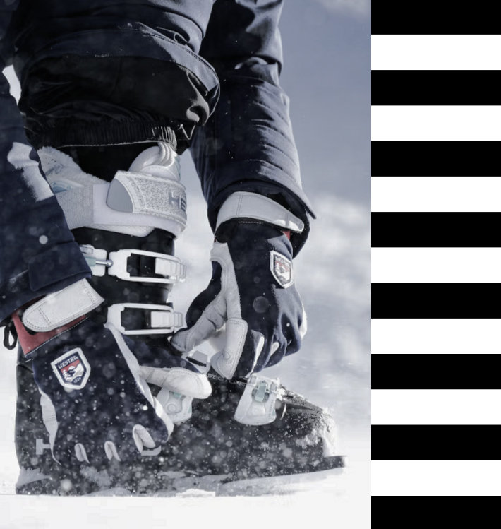 Schwarze und graue Winter-Skihandschuhe, hier in Kombination mit einer Funktionsjacke und Skischuhen im Schnee